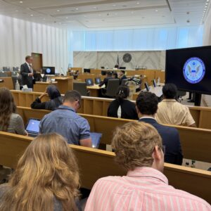 Audience seated in a federal courtroom watching a presenter at the front; a large screen shows the U.S. District Court seal.